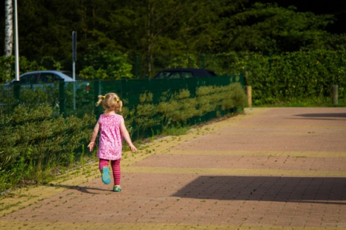 Child running to the playground and with the pink shirt having complementary colours to the hedge. Positioned according to the rule of thirds. Maybe a little to close in order to give the impression of an empty place with a single person in it.